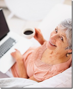 Happy old woman drinking coffee and using laptop